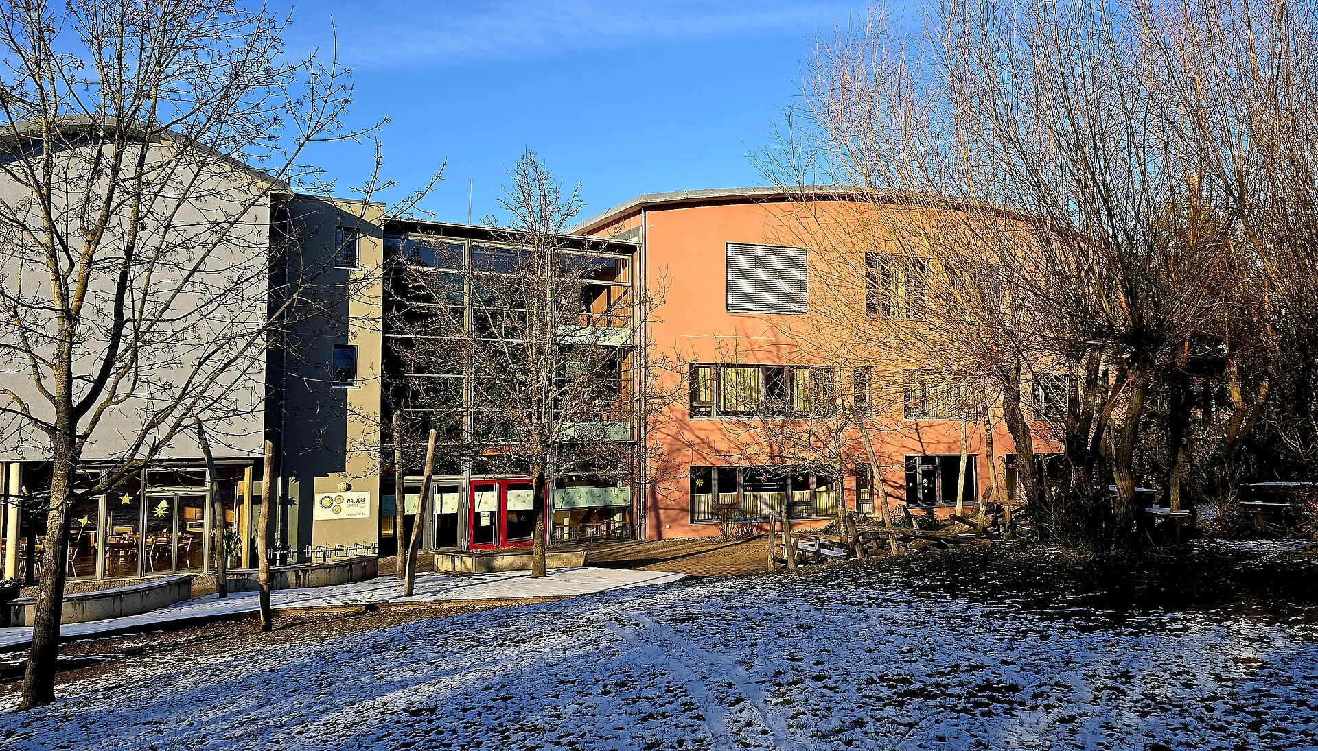 Almanya'da bir Waldorfschule'nin (Freie Waldorfschule Aalen) kışın karla kaplı bahçesindeki okul binası ve Waldorf tabelası