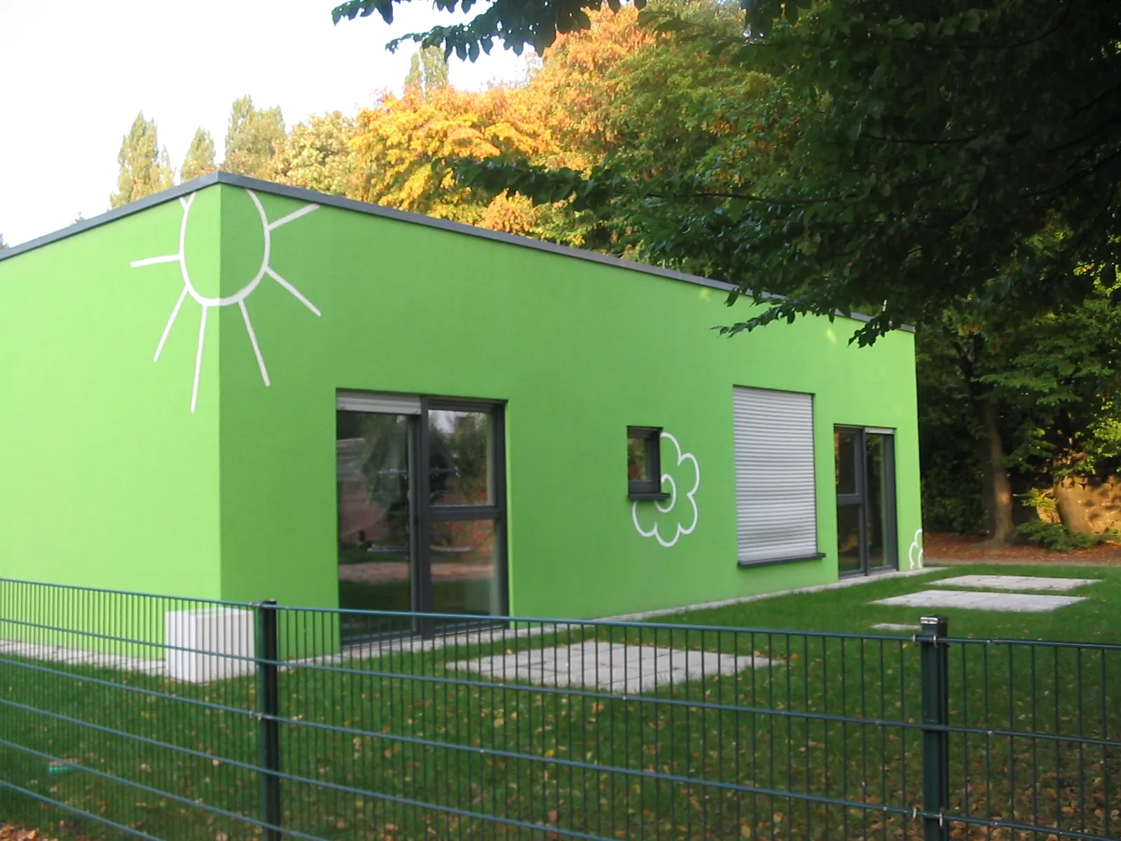 Almanya'da yeşil renkli, güneş ve bulut motifleriyle süslenmiş modern bir Kindergarten binasının dış cephesi