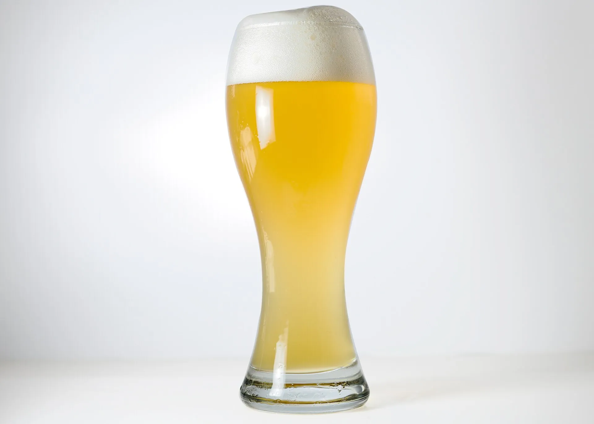 Beyaz köpük tabakasıyla dolu, bulanık altın sarısı rengiyle karakteristik bir Alman buğday birası (Weizenbier) bardağı
