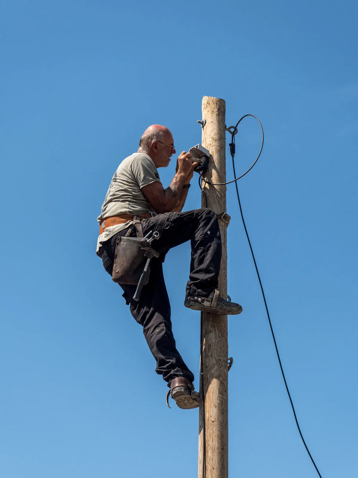 Elektrik teknisyeni direk üzerinde çalışırken kablo bağlantısı yapıyor